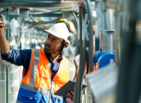 Gebäudetechniker in orangener Sicherheitsweste schraubt an den Geräten rum.