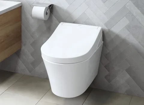 Das Bild zeigt ein wandhängendes TOTO Washlet RG mit geschlossenem Deckel, eingebettet in ein modern gestaltetes Bad mit grau gefliester Wand.