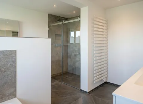 Zeitloses Badezimmer mit begehbarer Glasdusche, grauen Steinfliesen, weißem Waschtisch und Handtuchheizung.
