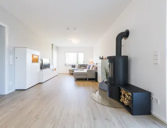 Heller Wohnraum mit Holzboden, schwarzen Kamin, weißen Möbeln und Fenster.