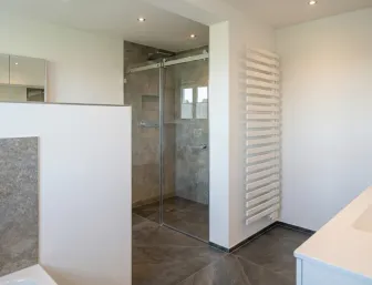 Zeitloses Badezimmer mit begehbarer Glasdusche, grauen Steinfliesen, weißem Waschtisch und Handtuchheizung.