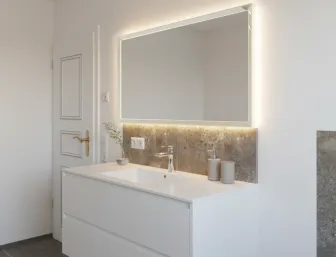 Hochwertiger Waschplatz mit weißem Möbelstück, Lichtspiegel, goldfarbenem Türgriff und klarer Linienführung.