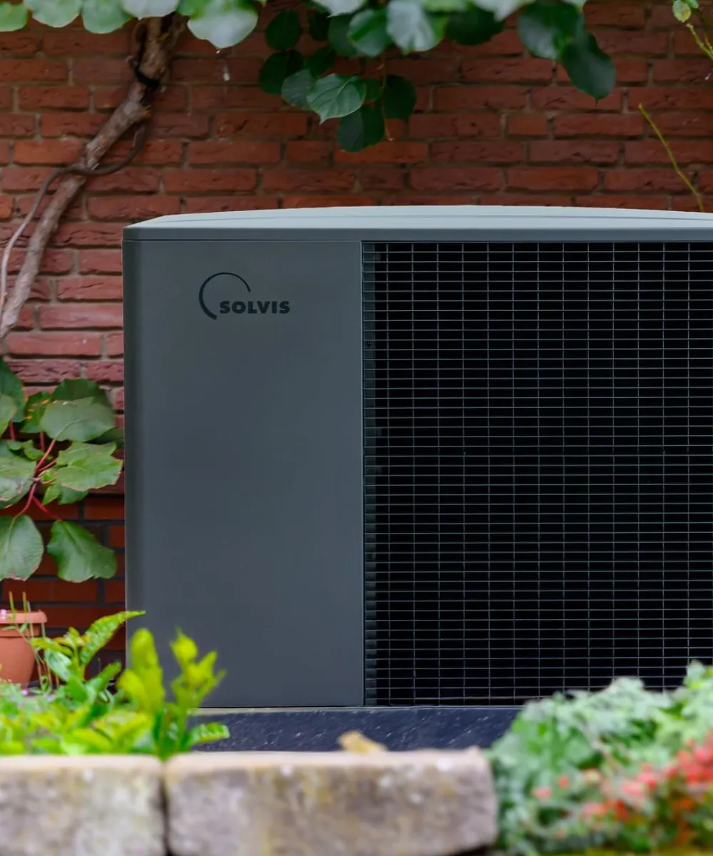 Wärmepumpe SolvisLea Pro von Solvis vor einer Ziegelwand in einem Garten.