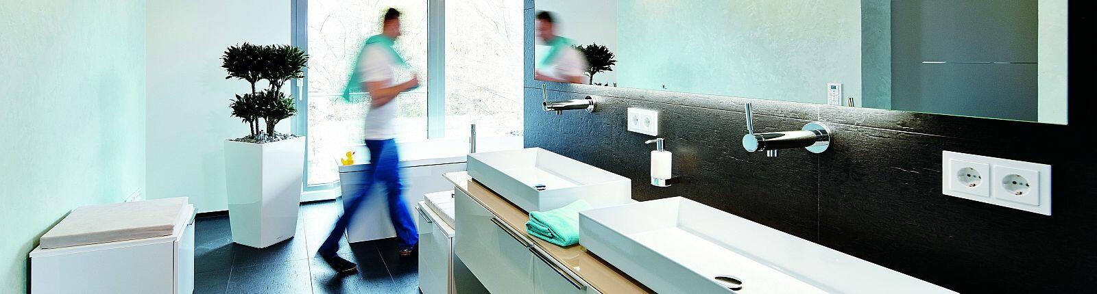 Mann mit Handtuch über Schulter läuft durchs Badezimmer